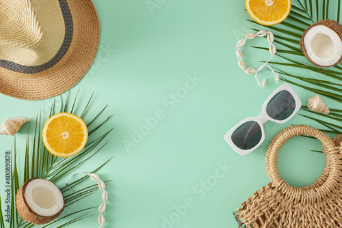 Summer stylish trend concept. Top view flat lay of bag, sunhat, shell bracelet, sunglasses, orange, coconut and palm leaves on turquoise background with empty space for text or advert