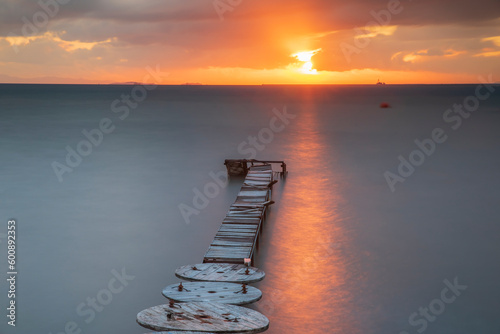 Wooden pier built into the sea and helping fishing, sunset colors and light