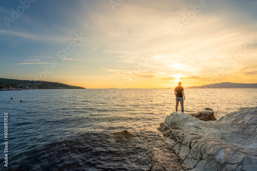 Young man standing on rocky beach at sunset time 
