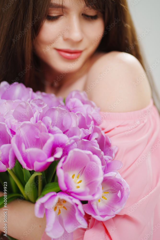 beautiful young brunette woman with long hair in pink with a bouquet of tulips. 