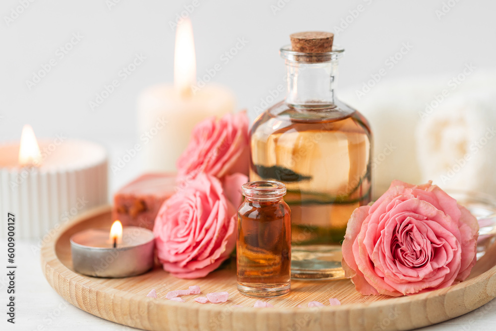 Aromatherapy. Concept of pure organic essential rose oil. Elixir with plant based floral or herbal ingredients. Pink flowers extract. Spa atmosphere with candle, towel. White background Aromatherapy. Concept of pure organic essential rose oil. Elixir with plant based floral or herbal ingredients. Pink flowers extract. Spa atmosphere with candle, towel. White background