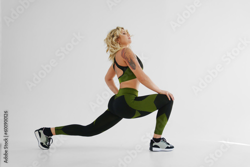 Fototapeta Naklejka Na Ścianę i Meble -  a blonde in a tracksuit makes stretching lunges on a white background