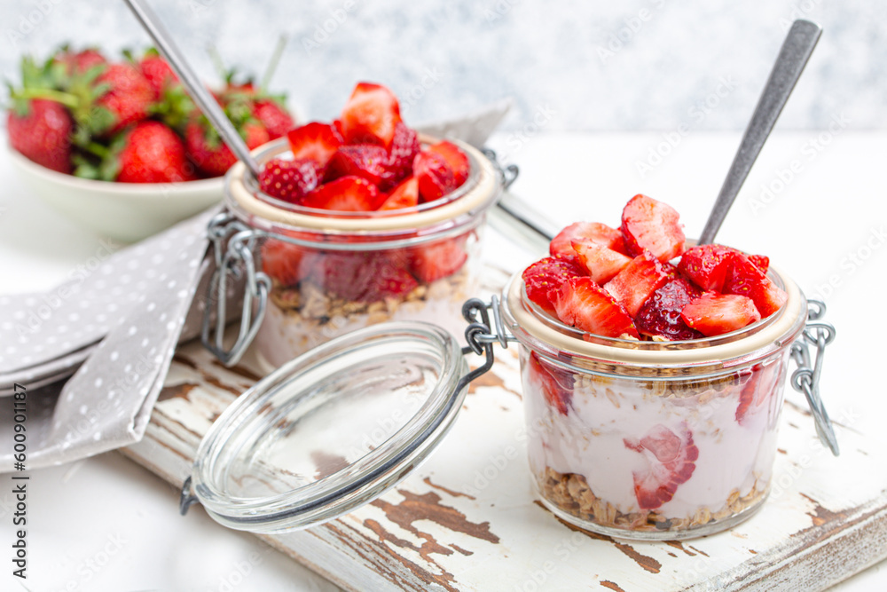 Parfait with Fresh Strawberries, Yoghurt and Crunchy Granola in Transparent Glass Mason Jars on White Rustic Wooden Background from Angle View, Healthy Breakfast or Light Summer Fruit Dessert Parfait with Fresh Strawberries, Yoghurt and Crunchy Granola in Transparent Glass Mason Jars on White Rustic Wooden Background from Angle View, Healthy Breakfast or Light Summer Fruit Dessert