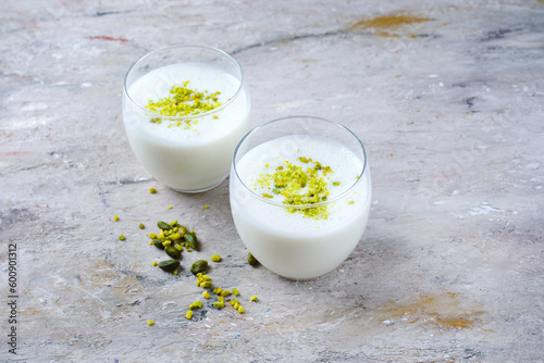 Traditional Indian lime lassi drink with dahi yogurt, lime and chopped pistachios served as close-up in a classical glass on a design plate with copy space photo
