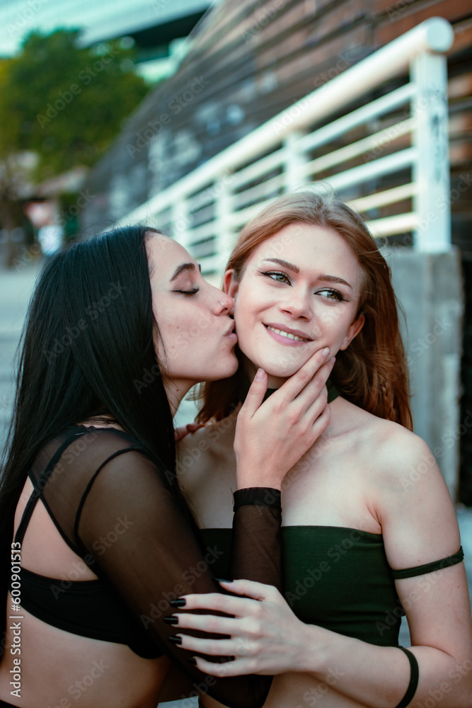 Latina best friends giving each other a kiss on the cheek in the center of the city Latina best friends giving each other a kiss on the cheek in the center of the city