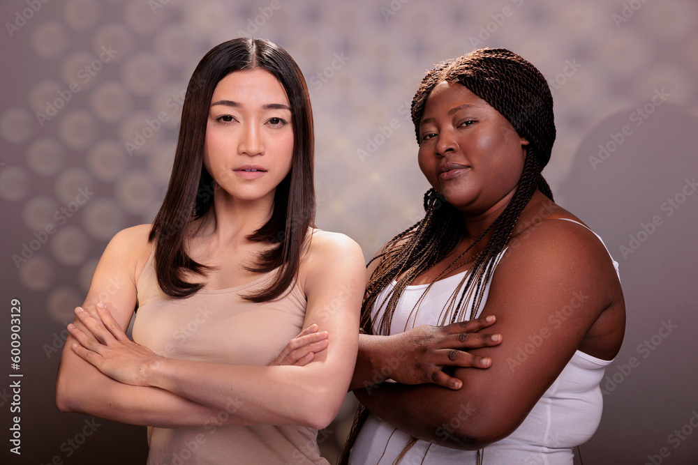 Confident diverse women posing with crossed hands, showing success gesture and looking at camera. African american and asian models with different body types standing with folded arms Confident diverse women posing with crossed hands, showing success gesture and looking at camera. African american and asian models with different body types standing with folded arms