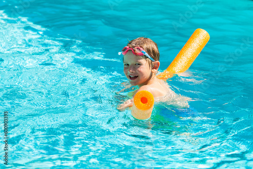 Oudoor summer activity. Concept of fun, health and vacation. Happy smiling boy five years old in swim glasses swim in the pool with noodle in hot summer day.