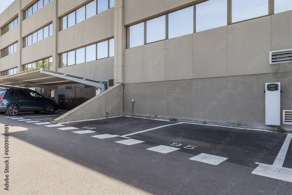 Uncovered parking with a fast charger for electric vehicles in the basement of an office building with a concrete facade Uncovered parking with a fast charger for electric vehicles in the basement of an office building with a concrete facade