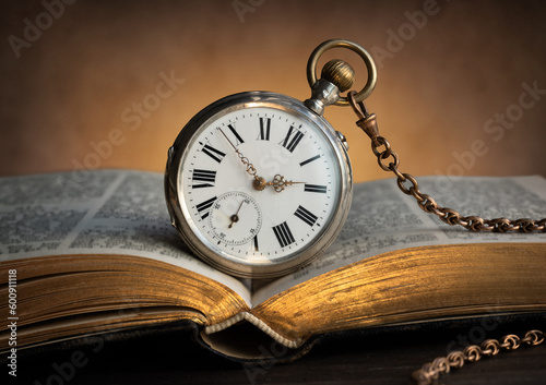 The clock lies on an old book. Clock as a symbol of time, the book is a symbol of knowledge and science. Concept of time, history, science, memory, information. Vintage watch, clock background.