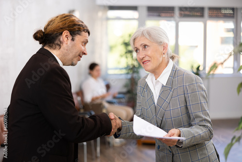Mature woman shaking hands with male colleague after making changes to expense document. Female coworker s handclasp was strong and friendly