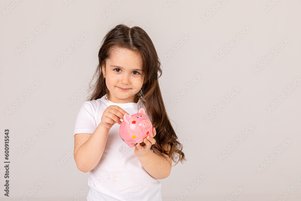 Positive girl in casual outfit laughing and saving money in piggy bank against white background Positive girl in casual outfit laughing and saving money in piggy bank against white background