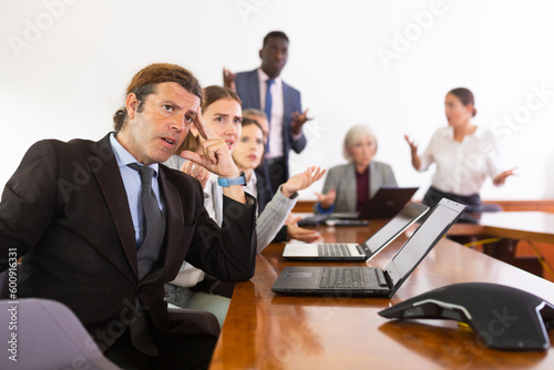 Nervous man in suit sitting at desk with group of coleagues during meeting.