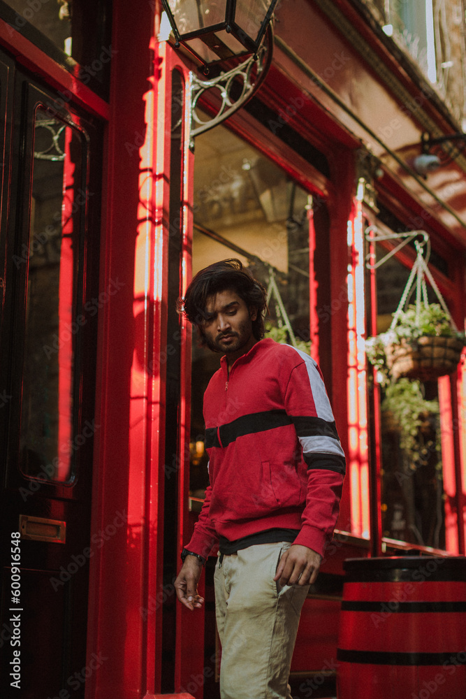 Fashion portrait of Indian Guy on the front of old building looking to the camera wearing a red shirt. Indian lifestyle and fashion. High quality photo