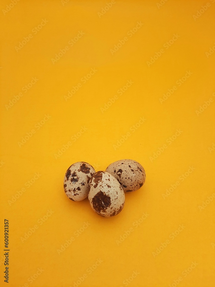 three quail eggs isolated on yellow background