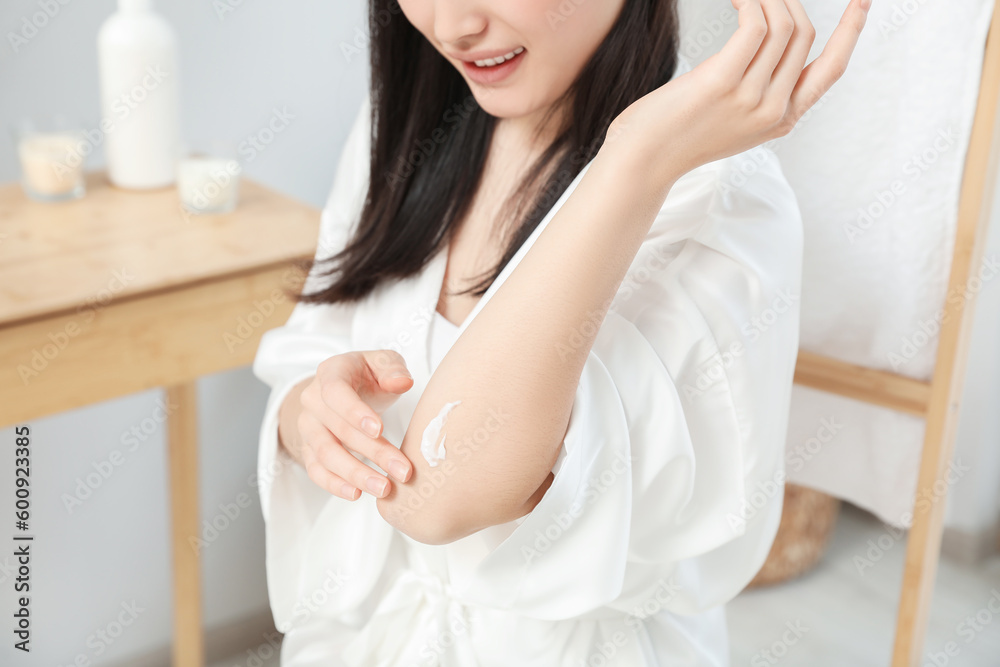 Young woman applying body cream on elbow in bathroom, closeup Young woman applying body cream on elbow in bathroom, closeup