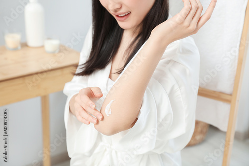 Young woman applying body cream on elbow in bathroom, closeup