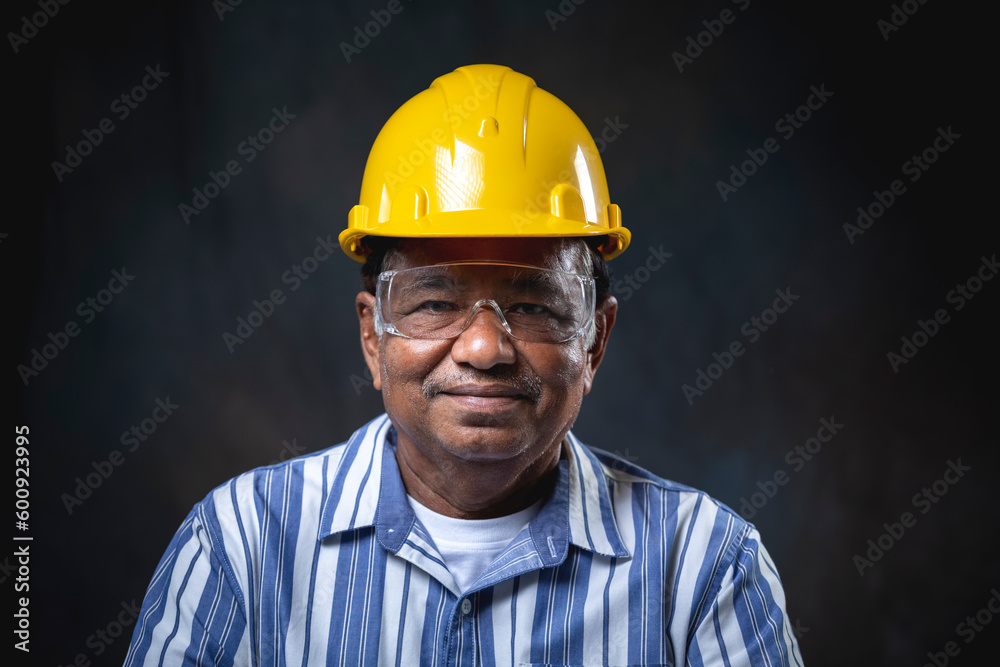 Portrait of architect or senior engineer, confident and smiling wearing yellow helmet looking at camera on black background in studio