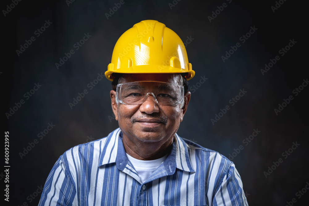 Portrait of architect or senior engineer, confident and smiling wearing yellow helmet looking at camera on black background in studio Portrait of architect or senior engineer, confident and smiling wearing yellow helmet looking at camera on black background in studio