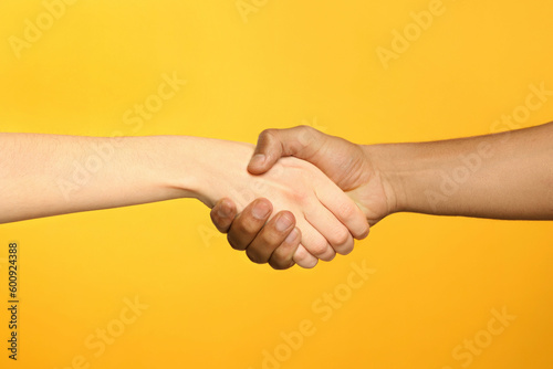 International relationships. People shaking hands on orange background, closeup