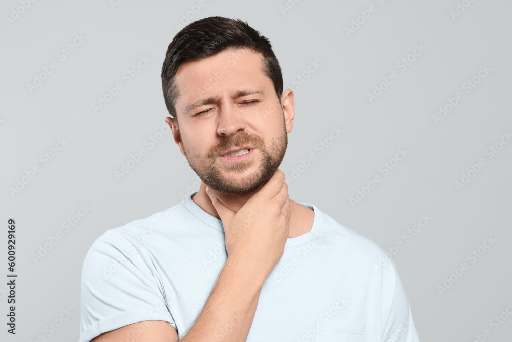 Man suffering from sore throat on light gray background Man suffering from sore throat on light gray background