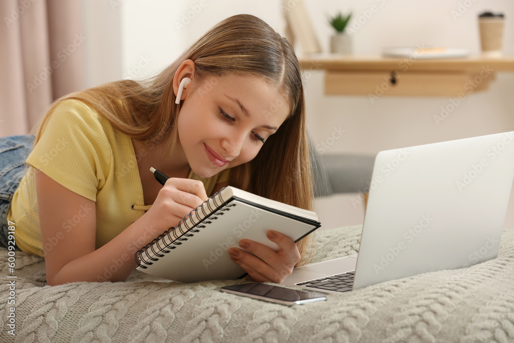 Teenage girl writing in notebook on bed at home Teenage girl writing in notebook on bed at home