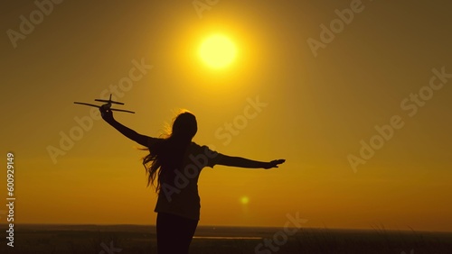 Happy girl running with plane hand sunset. hair wind. Game Teen Airplane Pilot. sun sky. girl runs happily across field. concept pilot aircraft. retarded motion. childhood dream.