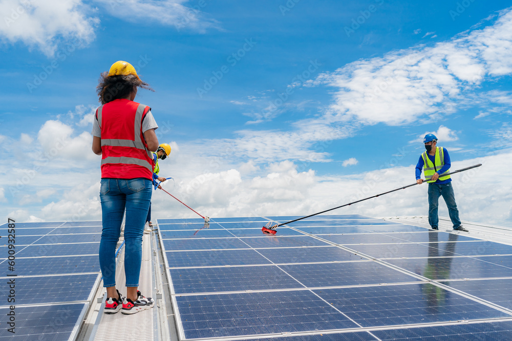 Professional worker cleaning solar panels with brush and washing with water on roof structure of building factory. Technician using mop to clean the dirty and dust, green electricity energy technology Professional worker cleaning solar panels with brush and washing with water on roof structure of building factory. Technician using mop to clean the dirty and dust, green electricity energy technology
