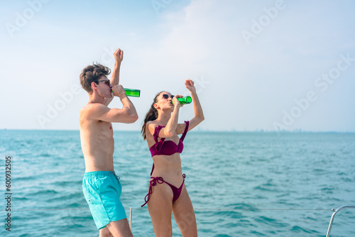 Portrait of happiness Caucasian couple drinking beer to party in yacht. Attractive man and woman hanging out celebrating anniversary in honeymoon trip while catamaran boat sailing during summer sunset
