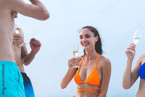 Friends group drink a champagne at outdoor party on yacht. Attractive young men and women hanging out, happy fun to celebrating holiday vacation trip on catamaran sailing boat, Summer relaxation time
