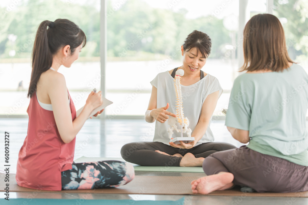 Fototapeta premium 骨盤・尾てい骨・骨格見本を見ながら説明するヨガインストラクターの先生と女性達（勉強会・講習会） 