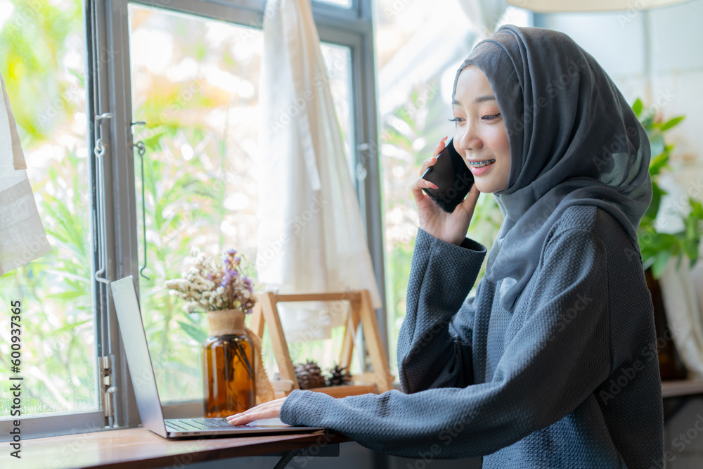 Modern Arab muslim girl in hijab using laptop and mobile phone at home, Cheerful girl sitting at desk and new order. Successful concept. Modern Arab muslim girl in hijab using laptop and mobile phone at home, Cheerful girl sitting at desk and new order. Successful concept.