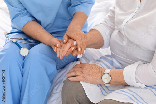 Young caregiver with senior woman holding hands in bedroom, closeup