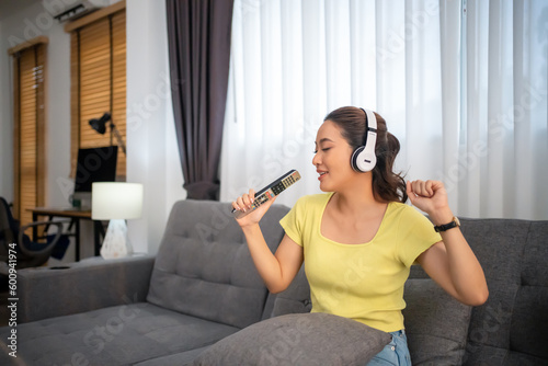 Woman wearing headphones and listening to music and singing happy at home on vacation.