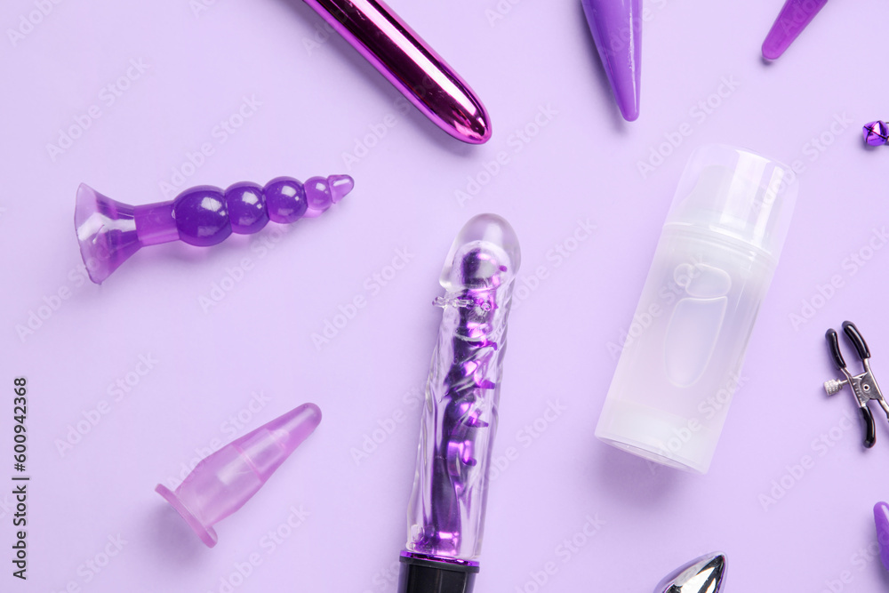 Bottle of lubricant with sex toys on lilac background
