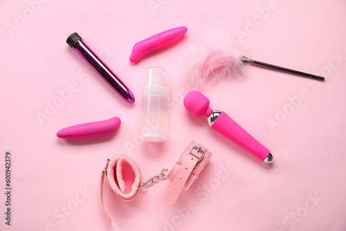 Bottle of lubricant and sex toys on pink background