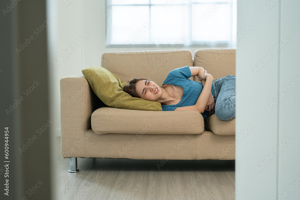 Young asian sick woman hands holding pressing lower abdomen. Medical or gynecological problems. Young woman suffering from abdominal pain on sofa at home healthcare concept. Stomach ache Young asian sick woman hands holding pressing lower abdomen. Medical or gynecological problems. Young woman suffering from abdominal pain on sofa at home healthcare concept. Stomach ache