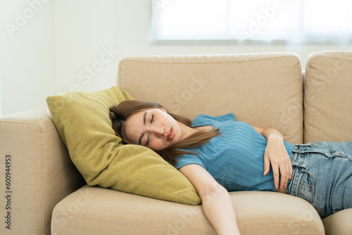 Asian caucasian woman lying on comfortable sofa in living room. Asian female fall asleep take a nap. Exhausted tired young woman. Cozy couch breath fresh air inside modern living room Leisure