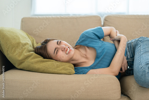 Young asian sick woman hands holding pressing lower abdomen. Medical or gynecological problems. Young woman suffering from abdominal pain on sofa at home healthcare concept. Stomach ache