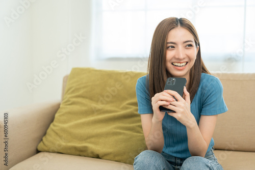 Asian woman using smartphone. Chatting video conference online sitting sofa in living room at home. Business Woman Shopping online store. Relax time at home