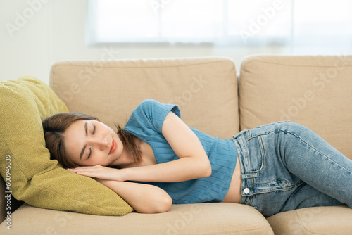 Asian caucasian woman lying on comfortable sofa in living room. Asian female fall asleep take a nap. Exhausted tired young woman. Cozy couch breath fresh air inside modern living room Leisure © Chanakon
