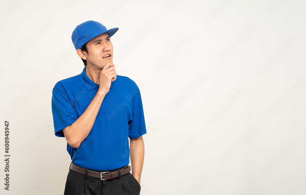 Happy delivery asian man in blue uniform standing thinking on isolated white background. Smiling male delivery service worker. Courier and shipping service.