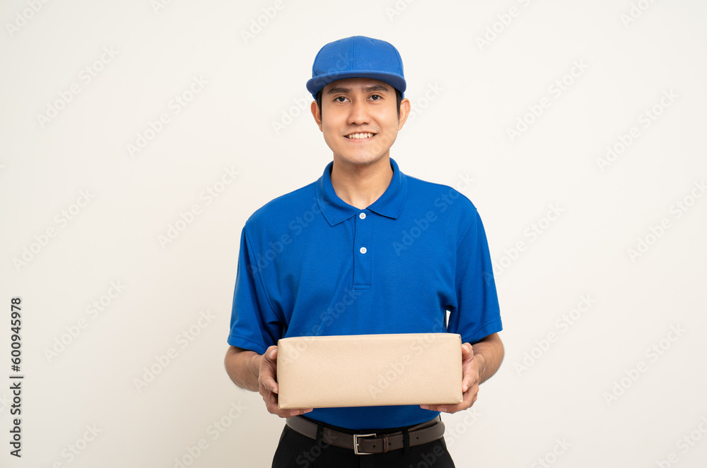 Happy delivery asian man in blue uniform standing holding box parcel cardboard on isolated white background. Smiling male service worker. Delivery courier and shipping service. Happy delivery asian man in blue uniform standing holding box parcel cardboard on isolated white background. Smiling male service worker. Delivery courier and shipping service.
