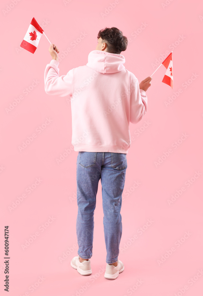 Young man with flags of Canada on pink background, back view Young man with flags of Canada on pink background, back view