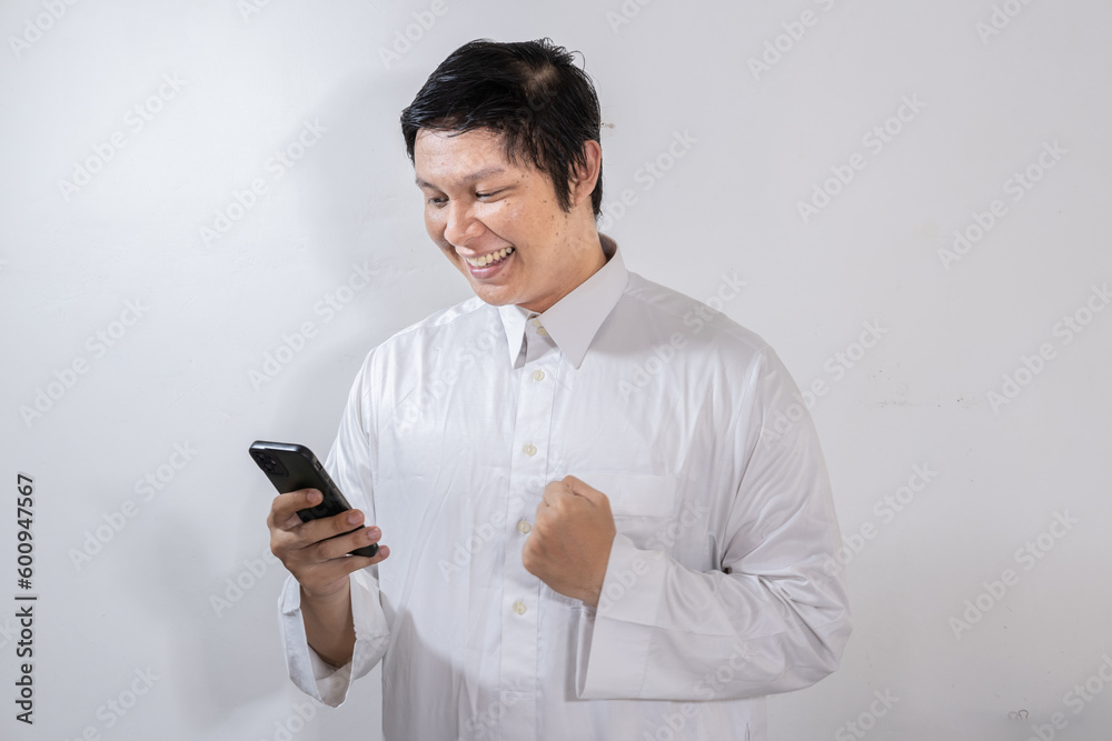 Happy looking Asian Muslim man showing joy while looking at his mobile phone Happy looking Asian Muslim man showing joy while looking at his mobile phone