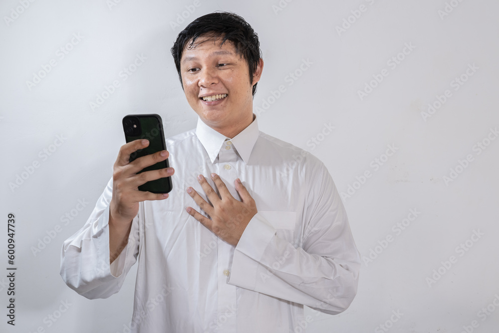 Happy looking Asian Muslim man showing joy while looking at his mobile phone Happy looking Asian Muslim man showing joy while looking at his mobile phone