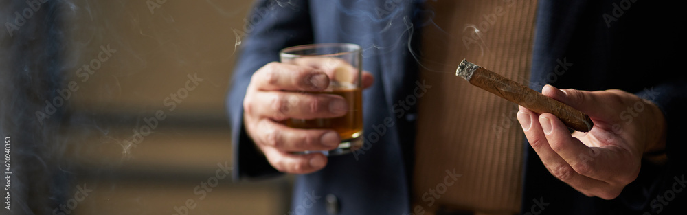 Close up shot of hand of mature man holding cigar and glass of w Close up shot of hand of mature man holding cigar and glass of w