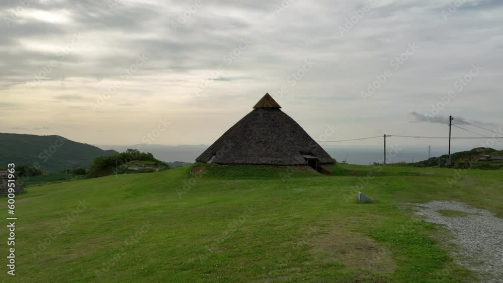 Ancient thatched roof hut on grassy hillside near coast in late afternoon Ancient thatched roof hut on grassy hillside near coast in late afternoon