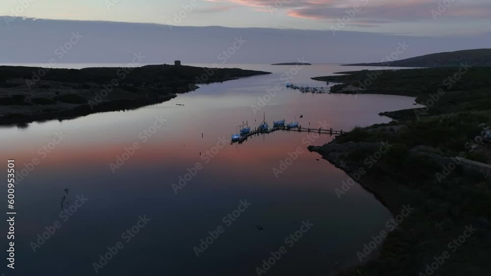 Aerial drone shot dropping behind hills as the reflection of fire sunset sets in the distance across the water. Aerial drone shot dropping behind hills as the reflection of fire sunset sets in the distance across the water.