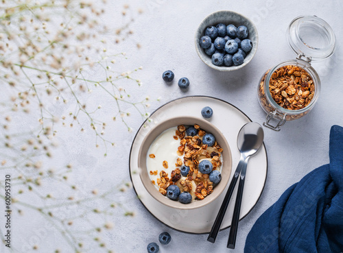 The concept of a healthy breakfast of yogurt, granola and fresh blueberry on a blue background with flowers. Homemade diet and protein food.