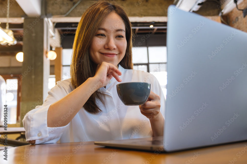 Portrait image of a young woman drinking coffee while working on laptop computer